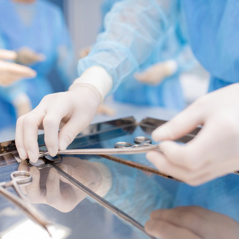 Gloved hands of surgeon or assistant taking one of sterile instruments