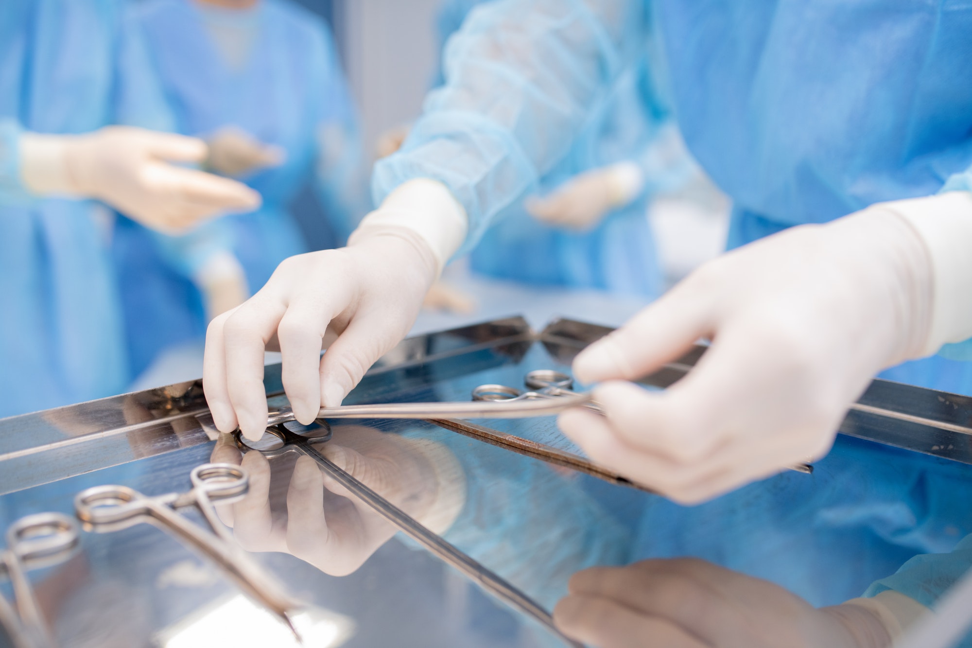 Gloved hands of surgeon or assistant taking one of sterile instruments
