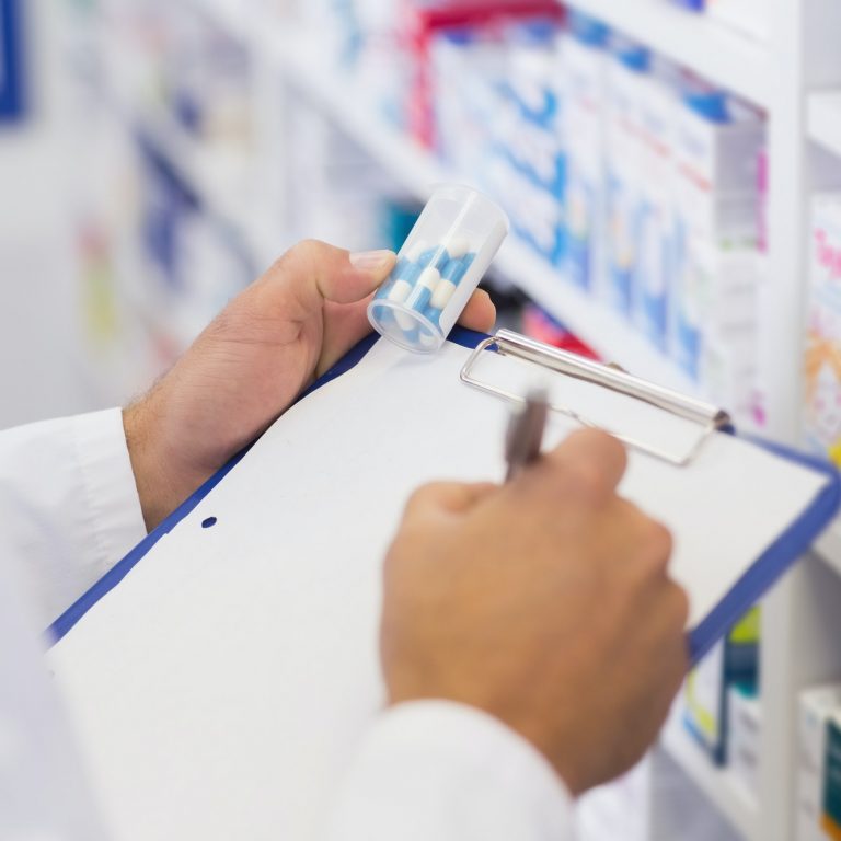 Pharmacist writing on clipboard and holding medicine jar at the hospital pharmacy