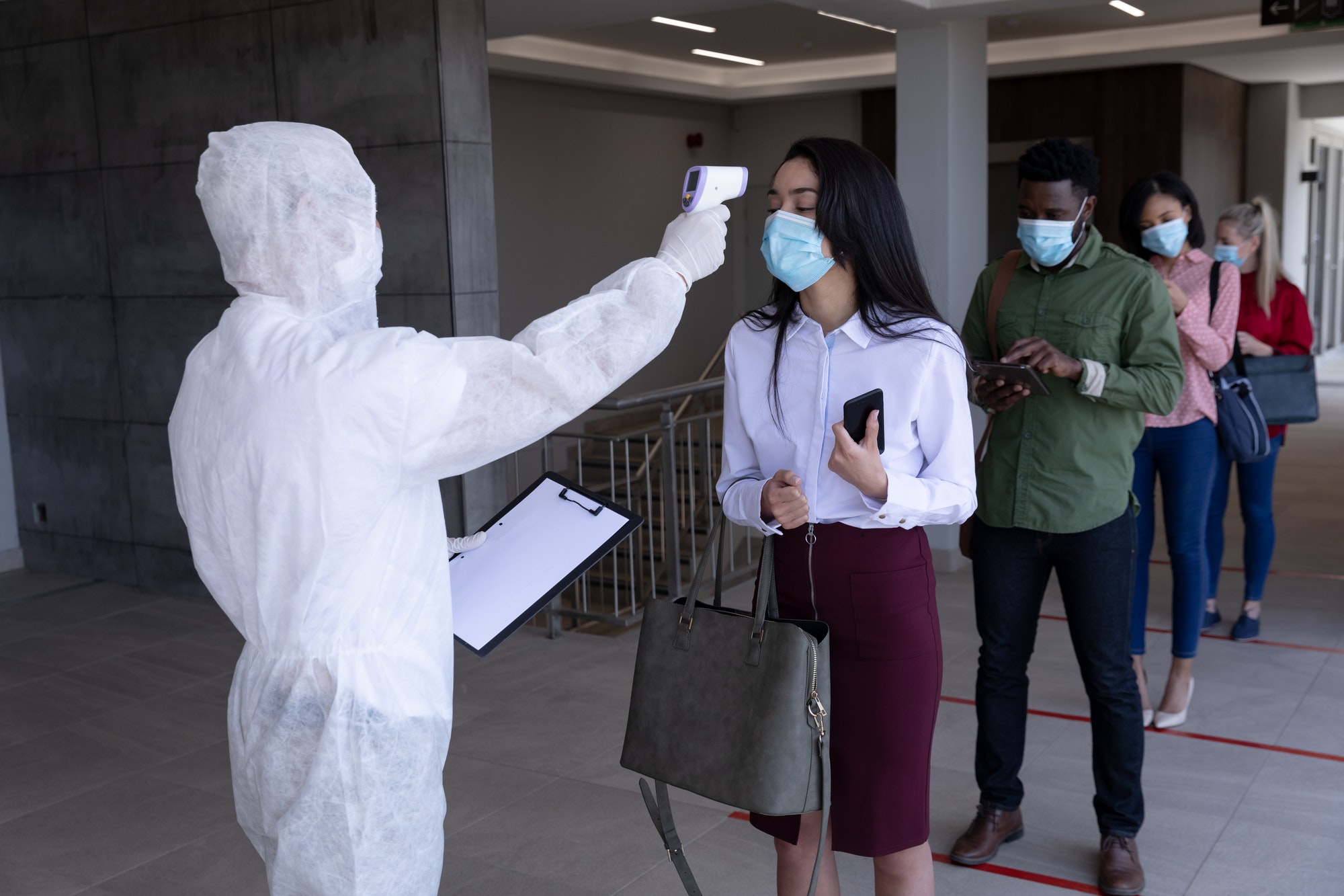 Health worker wearing protective clothes checking temperature of businesswoman