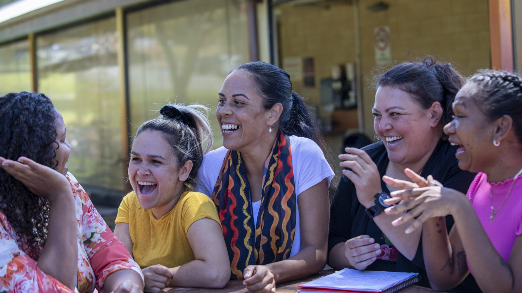 Young aboriginal female students sitting with their tutor outdoors in the sun in Australia.