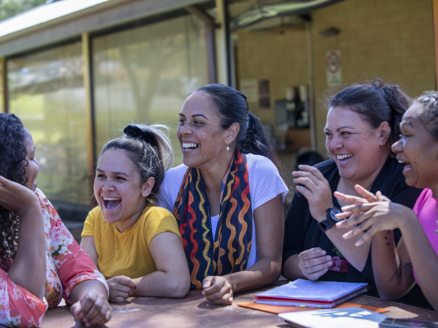 Young aboriginal female students sitting with their tutor outdoors in the sun in Australia.